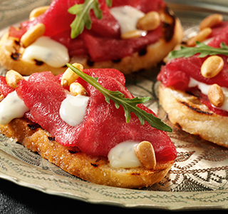 Crostini com carpaccio, rúcula e pinhão