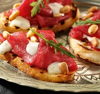 Crostini met carpaccio, rucola en pijnboompitten