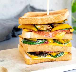 Pikante clubsandwich met plakjes cheddar kaas met sambal, salami, gegrilde paprika en courgette