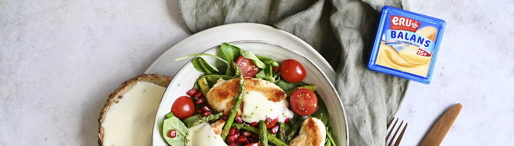 Maaltijdsalade met verschillende groenten, krokante kip, granaatappelpitjes en een dressing van belegen magere kaas met limoenrasp