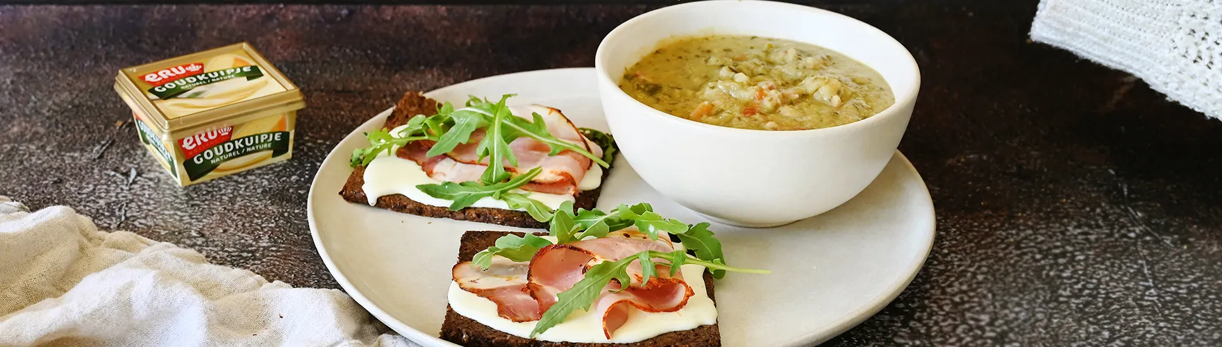 Erwtensoep en roggebrood belegd met roomzachte smeerkaas, katenspek en rucola