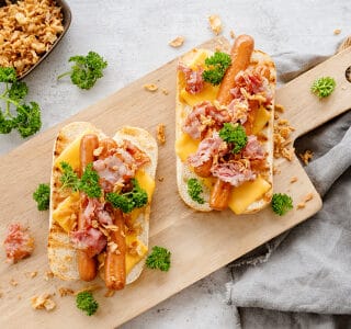 Broodje hotdog met cheddar kaas, bacon, gebakken uitjes en peterselie