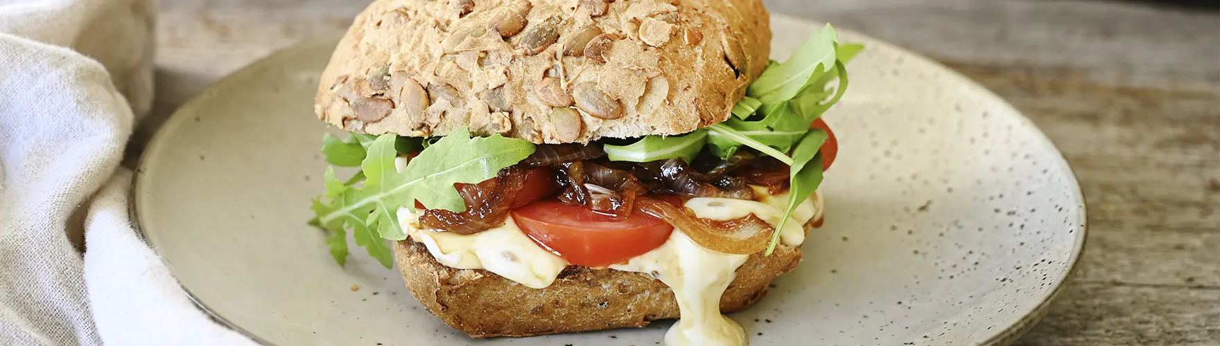 Pompoenbroodje met komijnekaas, tomaat, gekarameliseerde ui en rucola