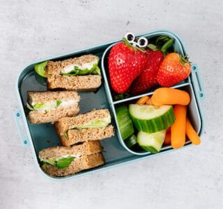 Kids lunchbox met aardbeien, komkommer, wortel en mini sandwiches met smeerkaas